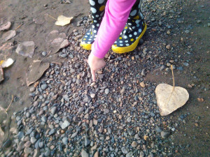 Child is not a pejorative A pink sleeved child's arm and hand points out a piece of quartzite in the center of a gravel patch