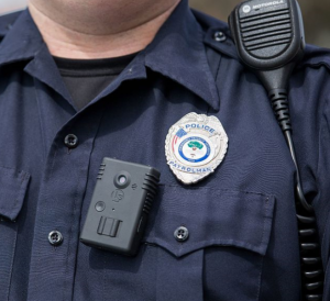 A uniformed cop's upper torso, showing a radio, badge and body camera.