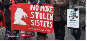Signs reading "No More Stolen Sisters" and "The Time for Truth is Now" Hands encircling a large red banner with white letters reading "No More Stolen Sisters" and a smaller sign reading "The Time for Truth is Now," from the 2019 Women's March on Washington