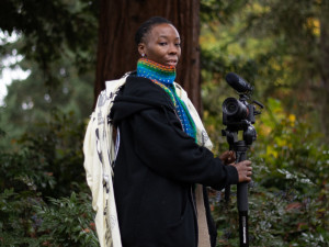 Kalimah Abioto standing outdoors with camera and tripod