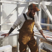 Farmer Brian Hulsey, wearing overalls and a sweater, looks serenely towards an empty shelf in an all white greenhouse.